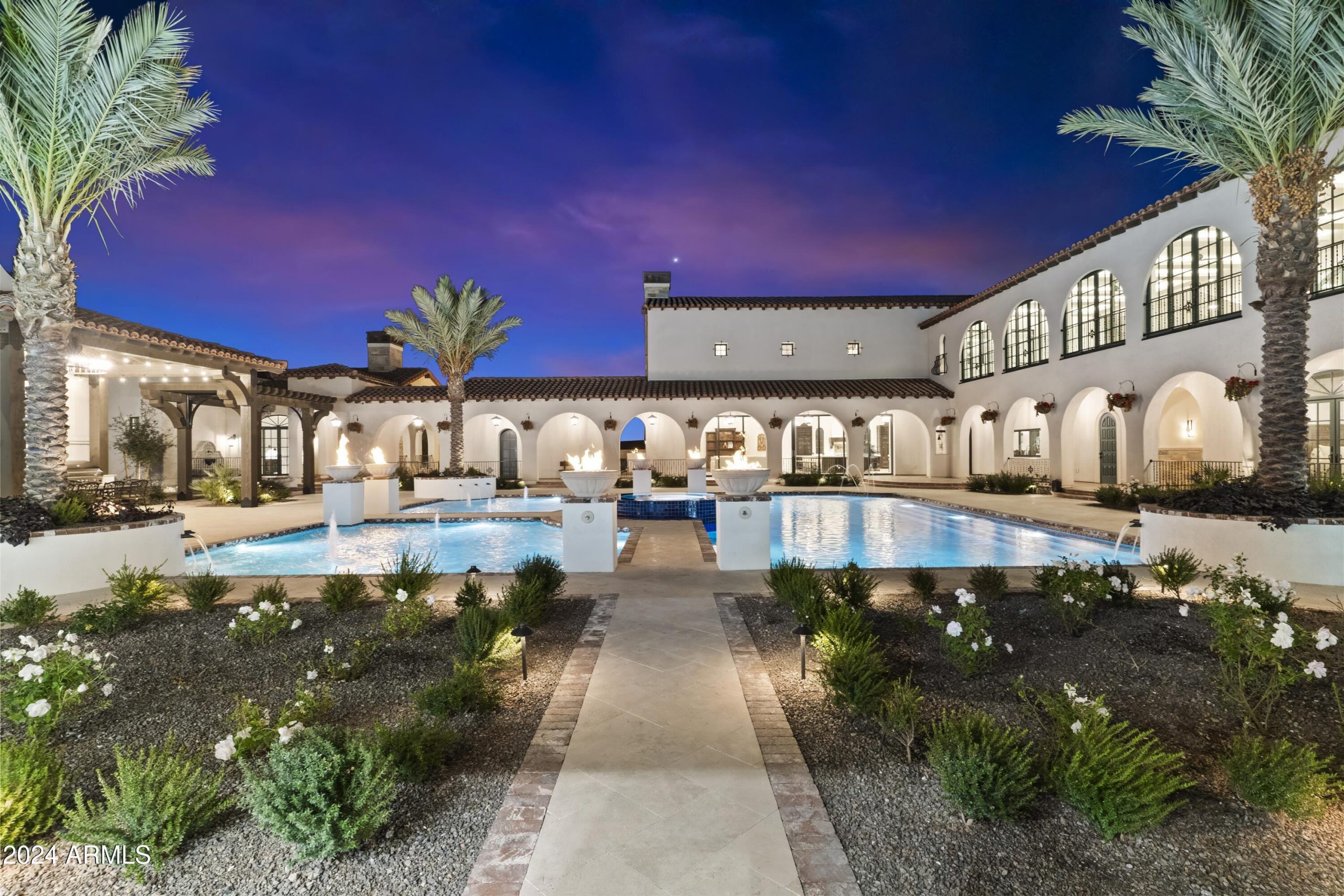 Stone walkways lead toward a luxury pool with fire accents.