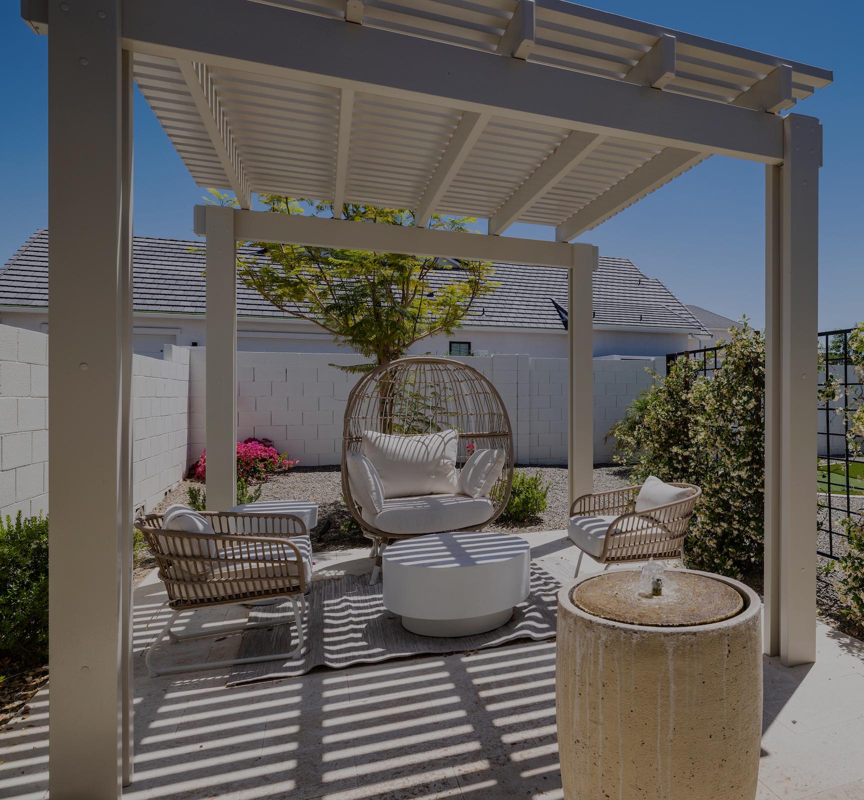 Louvered pergola covers wicker seating area and travertine stone patio